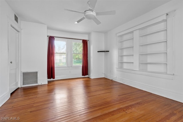 spare room with wood-type flooring, ceiling fan, and built in features