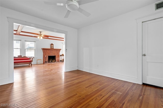 unfurnished living room with wood-type flooring, beamed ceiling, a brick fireplace, and ceiling fan