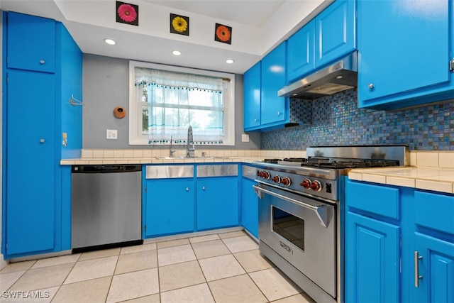 kitchen with blue cabinetry, light tile patterned floors, stainless steel appliances, and tile countertops