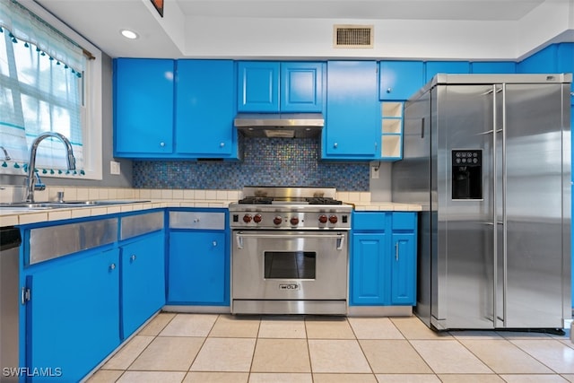 kitchen featuring blue cabinets, light tile patterned flooring, tasteful backsplash, stainless steel appliances, and sink