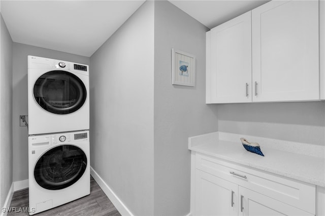 laundry area featuring cabinets, stacked washer / drying machine, and dark hardwood / wood-style flooring