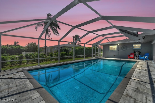 pool at dusk with glass enclosure and a patio