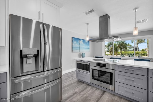 kitchen featuring white cabinets, pendant lighting, island range hood, appliances with stainless steel finishes, and hardwood / wood-style floors