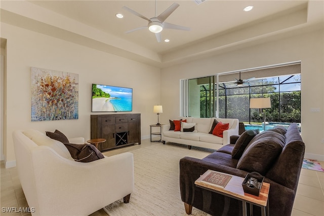 tiled living room with ceiling fan and a raised ceiling