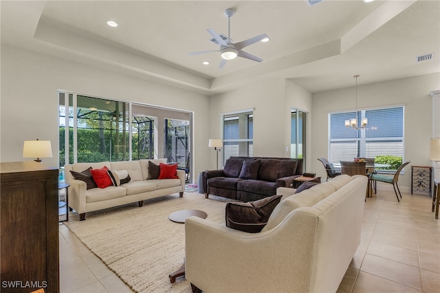 tiled living room with ceiling fan with notable chandelier and a tray ceiling