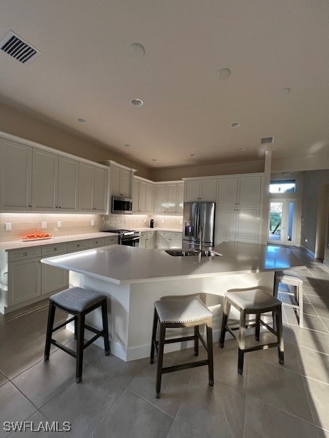 kitchen featuring white cabinetry, a kitchen bar, appliances with stainless steel finishes, light tile patterned floors, and a spacious island