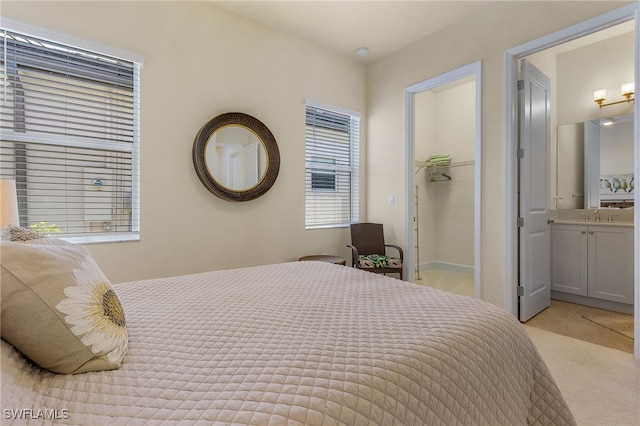 bedroom with light colored carpet, ensuite bath, sink, and a walk in closet