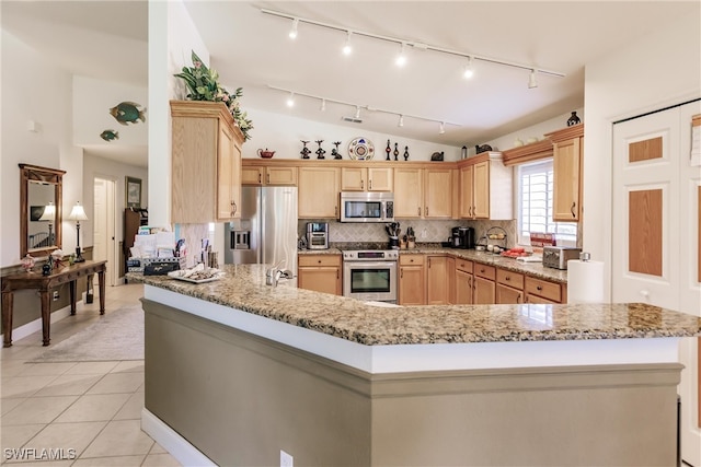 kitchen featuring lofted ceiling, light brown cabinetry, stainless steel appliances, light stone countertops, and backsplash