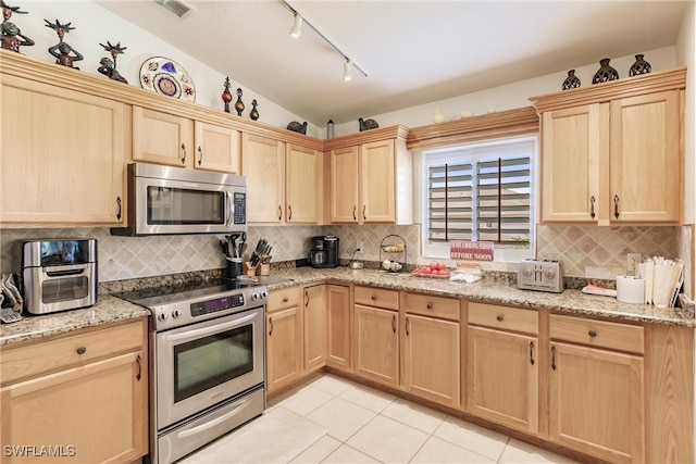 kitchen with light tile patterned flooring, light stone counters, vaulted ceiling, light brown cabinets, and appliances with stainless steel finishes