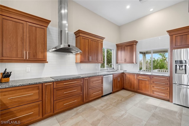 kitchen with sink, stone counters, wall chimney range hood, decorative backsplash, and appliances with stainless steel finishes