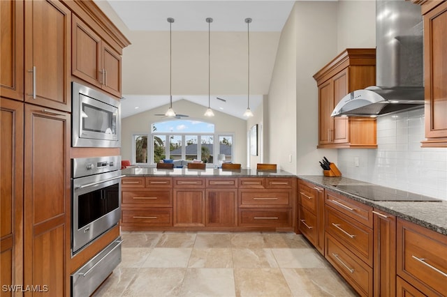 kitchen featuring appliances with stainless steel finishes, ceiling fan, decorative light fixtures, dark stone counters, and wall chimney range hood