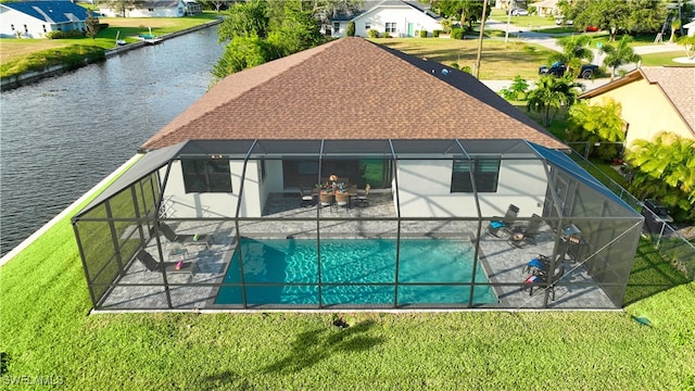 rear view of house with glass enclosure, a water view, a yard, and a patio area