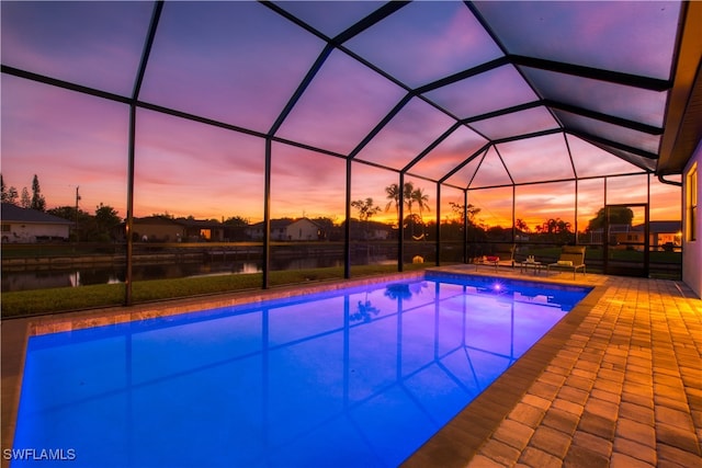 pool at dusk featuring a water view, a patio, and glass enclosure