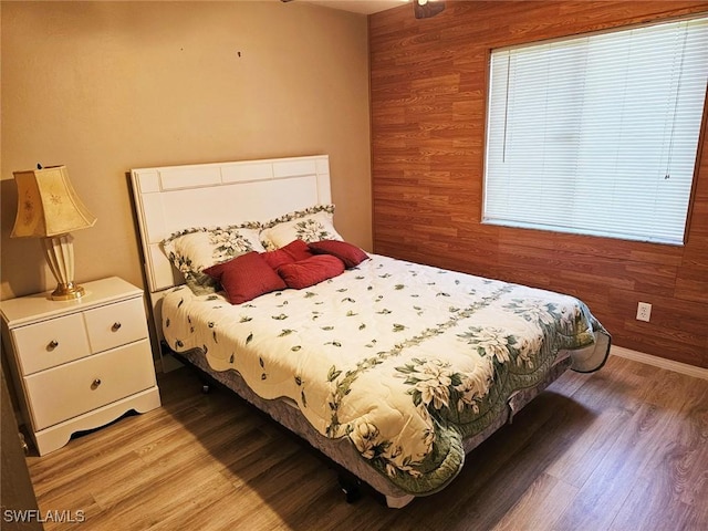 bedroom featuring light hardwood / wood-style floors, wood walls, and multiple windows