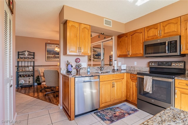 kitchen with appliances with stainless steel finishes, a textured ceiling, light wood-type flooring, and light stone countertops