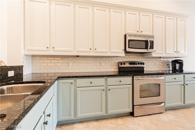 kitchen with dark stone countertops, backsplash, light tile patterned floors, stainless steel appliances, and sink