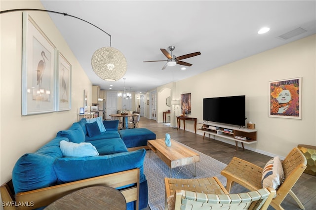 living room with dark hardwood / wood-style flooring and ceiling fan with notable chandelier