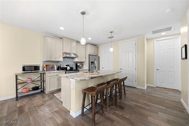 kitchen featuring pendant lighting, a center island with sink, a kitchen breakfast bar, light stone countertops, and stainless steel appliances