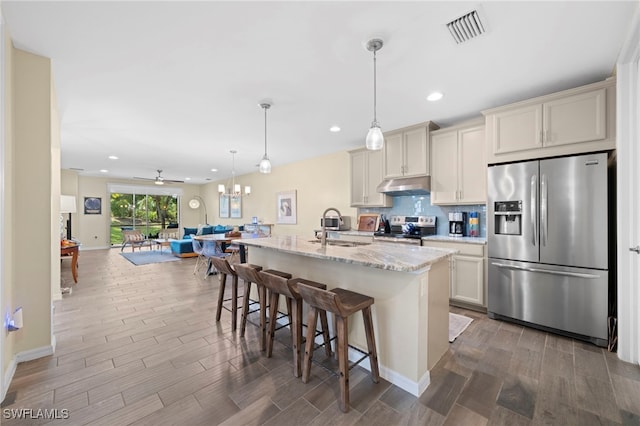 kitchen with a kitchen breakfast bar, sink, ceiling fan, light stone counters, and stainless steel appliances