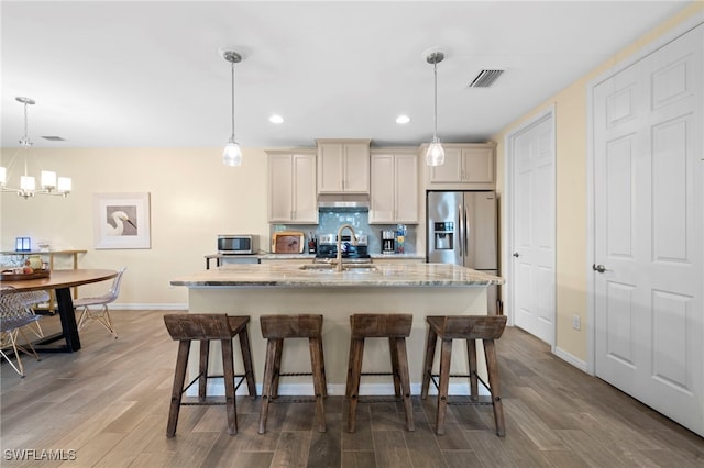 kitchen with a kitchen island with sink, sink, appliances with stainless steel finishes, tasteful backsplash, and decorative light fixtures