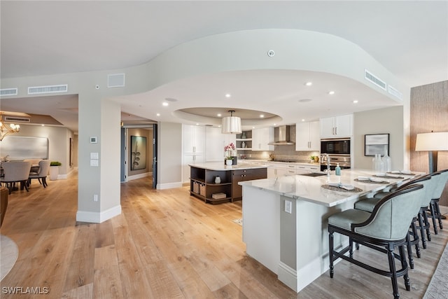 kitchen with a large island, black microwave, white cabinets, wall chimney range hood, and light hardwood / wood-style flooring