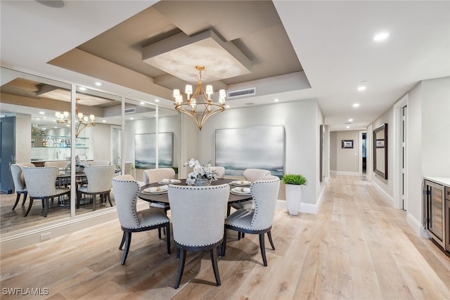 dining area with light wood-type flooring, a chandelier, a raised ceiling, and beverage cooler