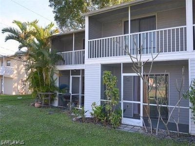 back of property featuring a lawn, a balcony, and a sunroom