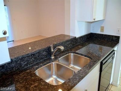 kitchen with dark stone counters, dishwasher, sink, white cabinetry, and light tile patterned floors