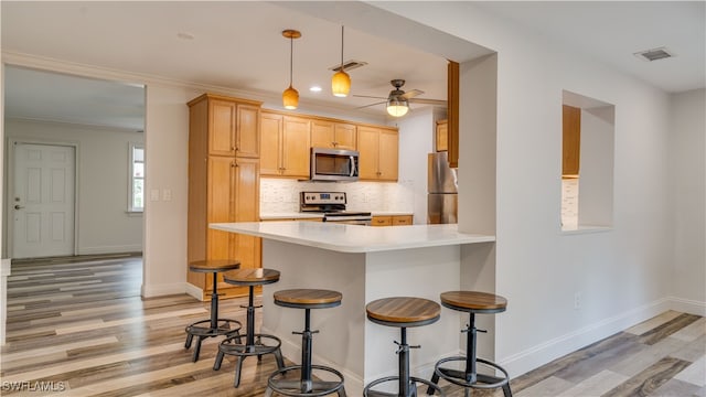 kitchen featuring kitchen peninsula, light hardwood / wood-style flooring, a kitchen breakfast bar, appliances with stainless steel finishes, and ceiling fan