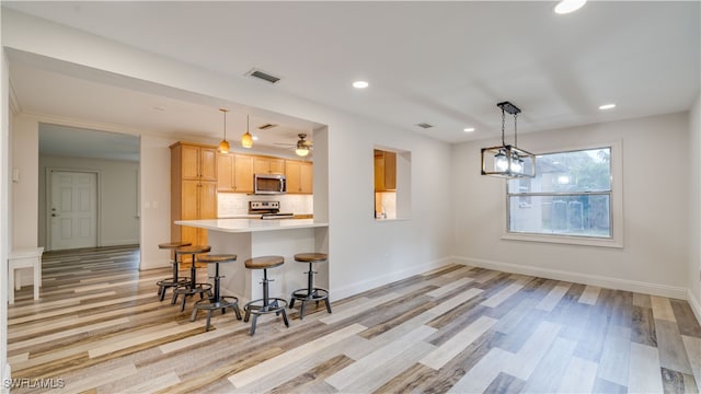 kitchen featuring pendant lighting, light hardwood / wood-style floors, stainless steel appliances, backsplash, and light brown cabinets