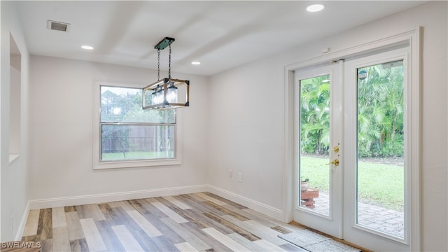 unfurnished dining area featuring light hardwood / wood-style flooring, a wealth of natural light, a notable chandelier, and french doors