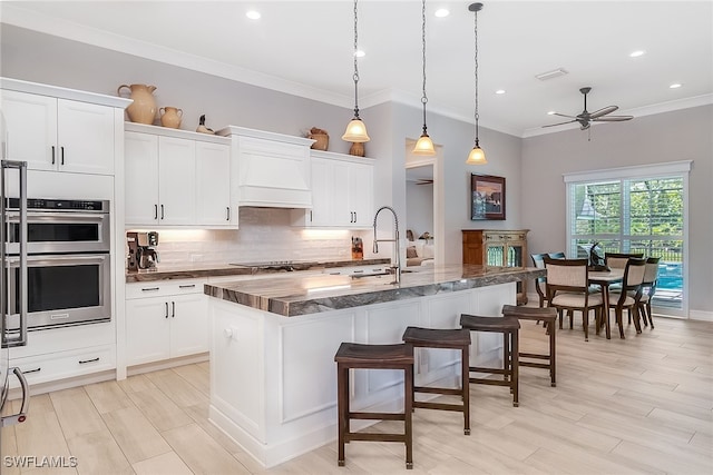 kitchen featuring ceiling fan, pendant lighting, a kitchen island with sink, double oven, and a kitchen breakfast bar