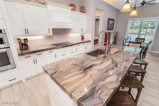 kitchen with ceiling fan, pendant lighting, a center island with sink, and a kitchen bar