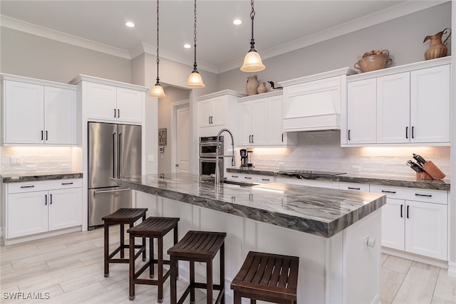 kitchen with decorative light fixtures, an island with sink, stainless steel appliances, and white cabinets