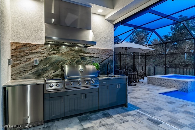 patio terrace at dusk with glass enclosure, an in ground hot tub, area for grilling, a grill, and sink