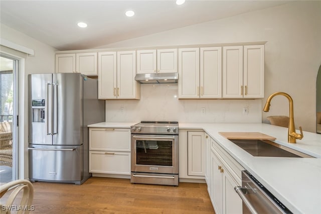 kitchen with sink, vaulted ceiling, light hardwood / wood-style flooring, decorative backsplash, and appliances with stainless steel finishes