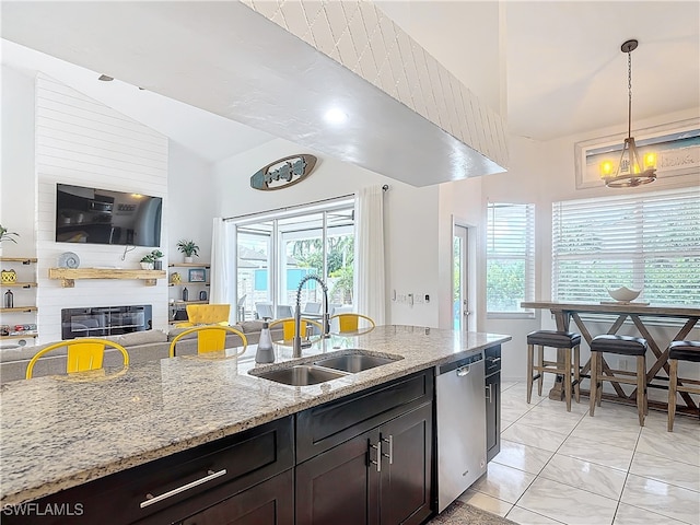 kitchen with hanging light fixtures, sink, stainless steel dishwasher, a large fireplace, and light stone countertops