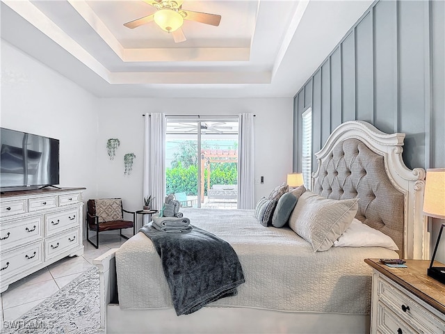 bedroom featuring access to outside, light tile patterned floors, a tray ceiling, and ceiling fan