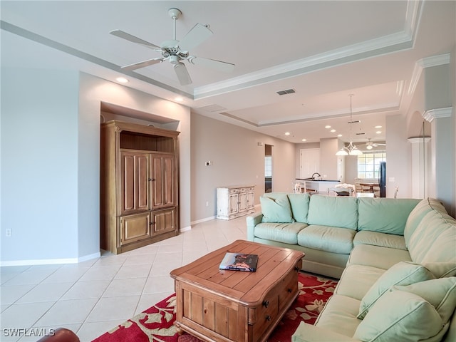 tiled living room with ceiling fan, a raised ceiling, and ornamental molding