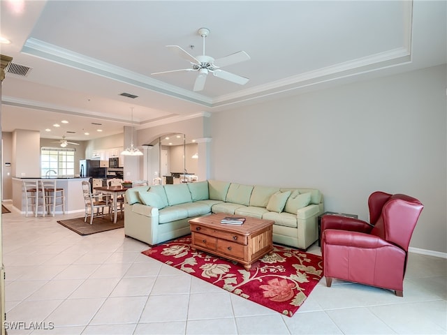 tiled living room with decorative columns, crown molding, ceiling fan, and a raised ceiling