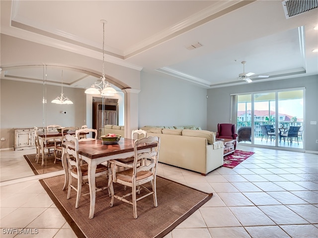 tiled dining area with ornate columns, ceiling fan with notable chandelier, crown molding, and a tray ceiling