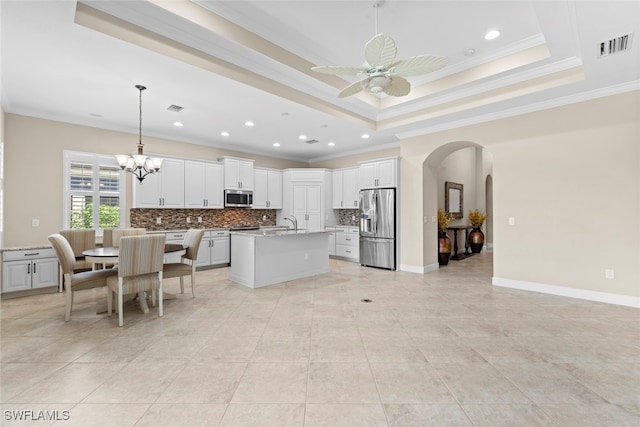 kitchen with tasteful backsplash, stainless steel appliances, pendant lighting, white cabinets, and a kitchen island with sink