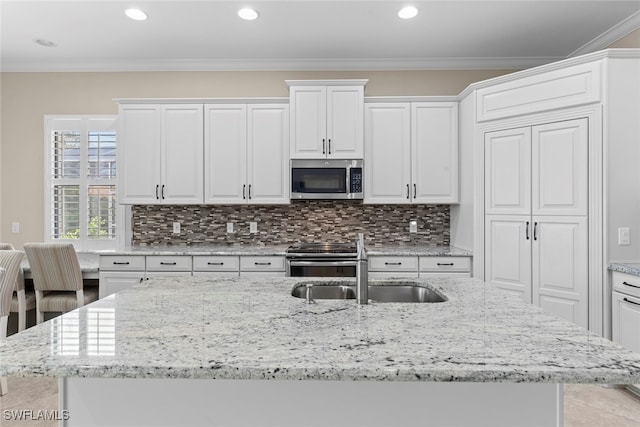 kitchen featuring white cabinetry, stainless steel appliances, crown molding, decorative backsplash, and a kitchen island with sink