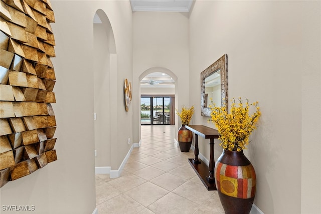 hallway with a towering ceiling, crown molding, and light tile patterned flooring