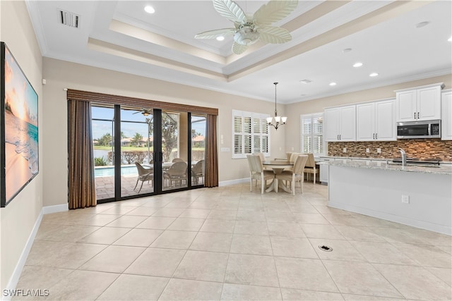 kitchen with crown molding, tasteful backsplash, ceiling fan with notable chandelier, white cabinets, and light stone counters