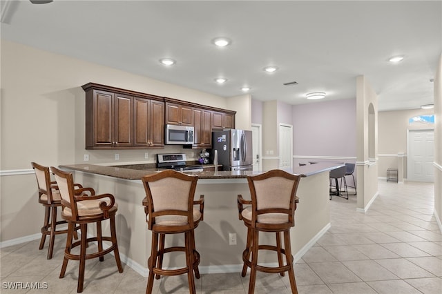 kitchen with appliances with stainless steel finishes, kitchen peninsula, dark stone counters, and a breakfast bar area