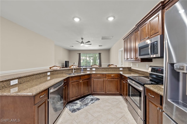 kitchen featuring kitchen peninsula, stainless steel appliances, sink, stone counters, and ceiling fan