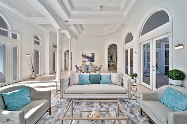 living room featuring french doors, a towering ceiling, ornamental molding, and decorative columns