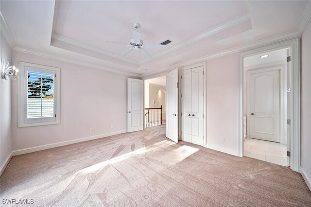 unfurnished bedroom featuring ceiling fan, a raised ceiling, ornamental molding, and light colored carpet