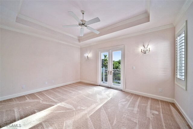 empty room with french doors, a raised ceiling, ornamental molding, and light colored carpet